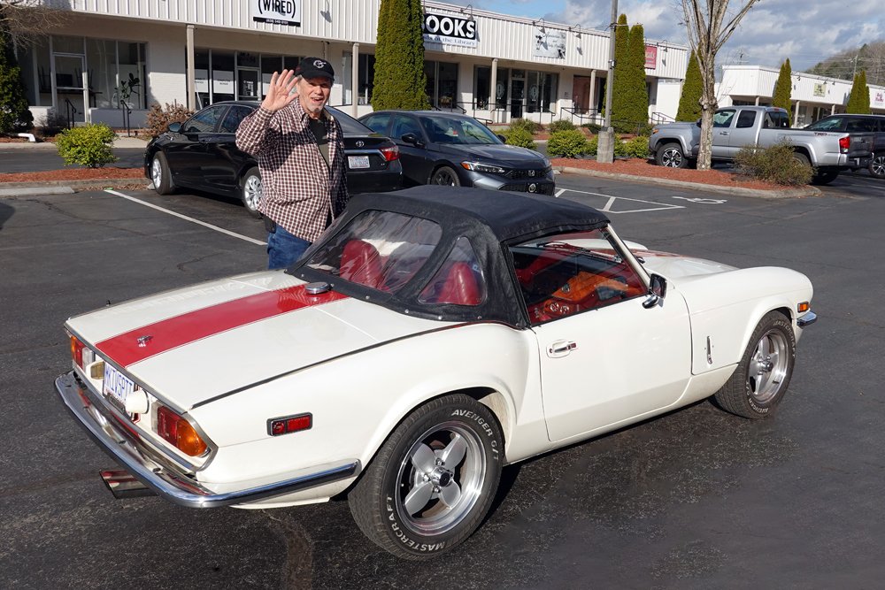 Triumph Spitfire Mk IV parked outside a storefront with its owner alongside